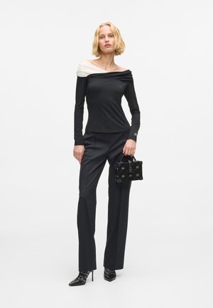 Czarny top z długim rękawem z białymi opadającymi ramionami, w połączeniu z czarnymi dopasowanymi spodniami i małą czarną torebką w wzór. Czarne szpilki.