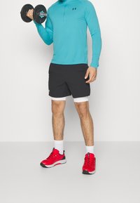 Sportoutfit mit einem türkisfarbenen Langarmshirt, schwarzen Shorts mit weißen Akzenten und roten Sneakers mit schwarz-weißen Details.