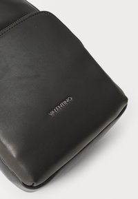 Borsa a pochette nera in pelle con una texture liscia. Presenta cuciture sottili e un logo argento "Valentino" sul davanti. Forma compatta.