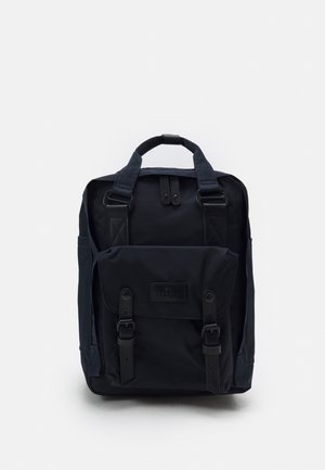 Sac à dos carré noir avec poche avant à rabat, sécurisé par deux sangles à boucle et double poignée de transport sur le dessus.