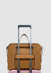 Bruine leren handtas bevestigd aan een roze koffer met harde schaal en uitgetrokken zilveren telescopische handvat tegen een effen grijze achtergrond.