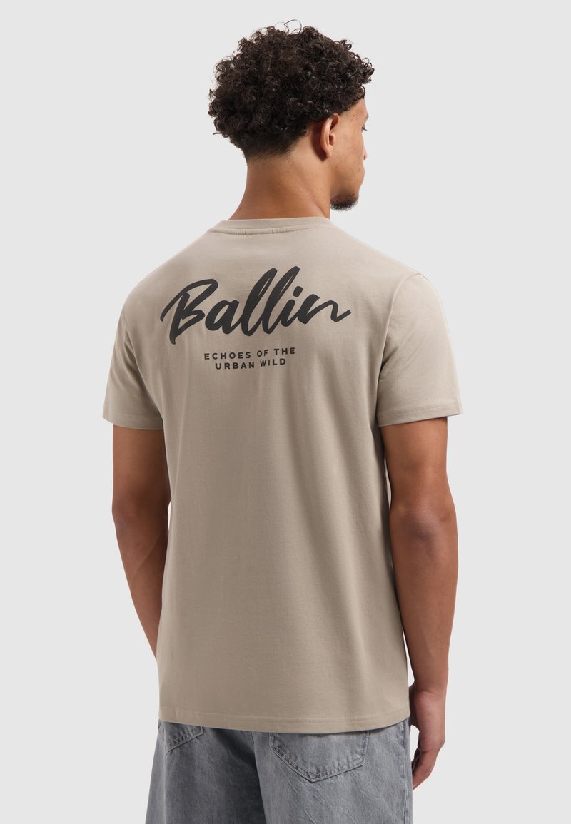 Beige katoenen t-shirt met korte mouwen, ronde halslijn en zwarte grafische tekst op de achterkant met de woorden "Ballin" en "ECHOES OF THE URBAN WILD."