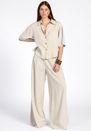 Beige linnen overhemd met korte mouwen, voorzien van een knoopsluiting en twee zakken, gecombineerd met bijpassende wijde broek met een zachte textuur.
