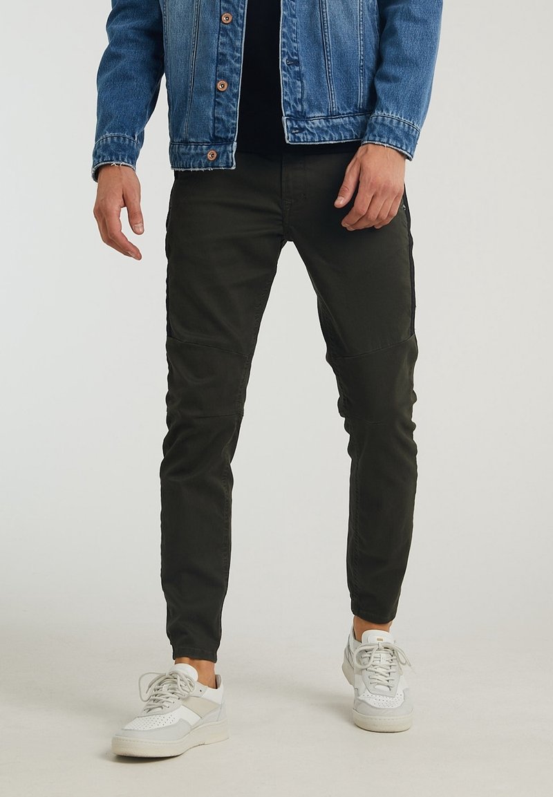 Mörkgröna slim-fit byxor med knäpaneler, kombinerade med en jeansjacka och vita sneakers. Mjukt tyg med en subtil glans.