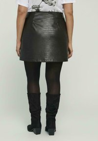 Zwarte mini-rok van kunstleer met krokodillenstructuur, gecombineerd met ondoorzichtige zwarte panty's en zwarte, slouchy kniehoge laarzen met blokhakken.