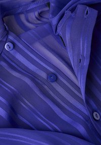 Camicia viola trasparente con righe verticali, due bottoni rotondi sul davanti, trama liscia e design leggero e fluente.