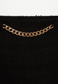 Tessuto nero con una superficie texturizzata che presenta un accento di catena dorata nella parte superiore. La catena ha anelli intrecciati e una finitura lucida.