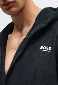 Robe preto com capuz em tecido macio com acabamento texturizado. Apresenta um logótipo "BOSS" branco com detalhes coloridos no lado esquerdo.