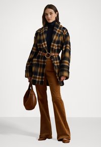 Geruite, oversized wollen blend jas in bruin, zwart en goud, met een ceintuur in de taille. Bruine corduroy flared broeken en een bruine handtas.
