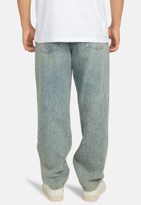 Lichtblauwe denim wijdere jeans zijn voorzien van een vervaagde wassing, twee achterzakken en zijn gestyled met een witte T-shirt en beige sneakers.