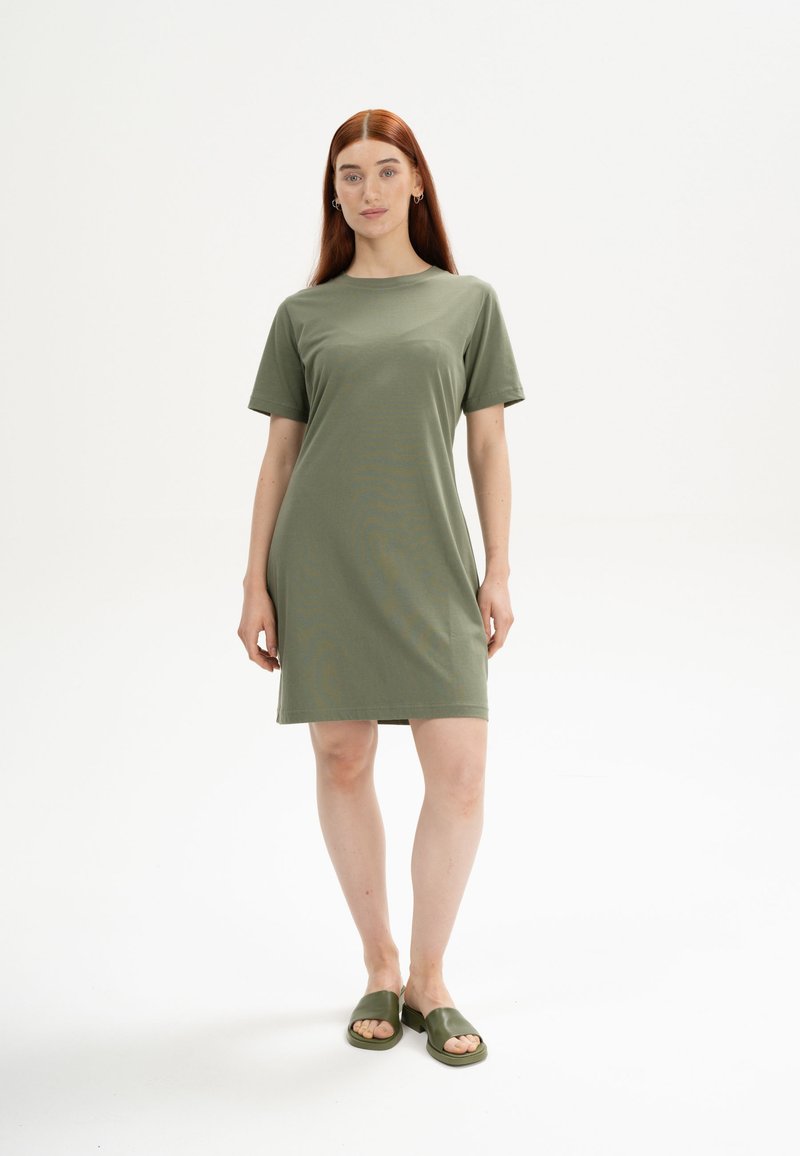 Olivenfarbenes Kurzarmkleid aus weichem Stoff, mit einem einfachen Rundhalsausschnitt und geradem Schnitt, kombiniert mit passenden Sandalen.