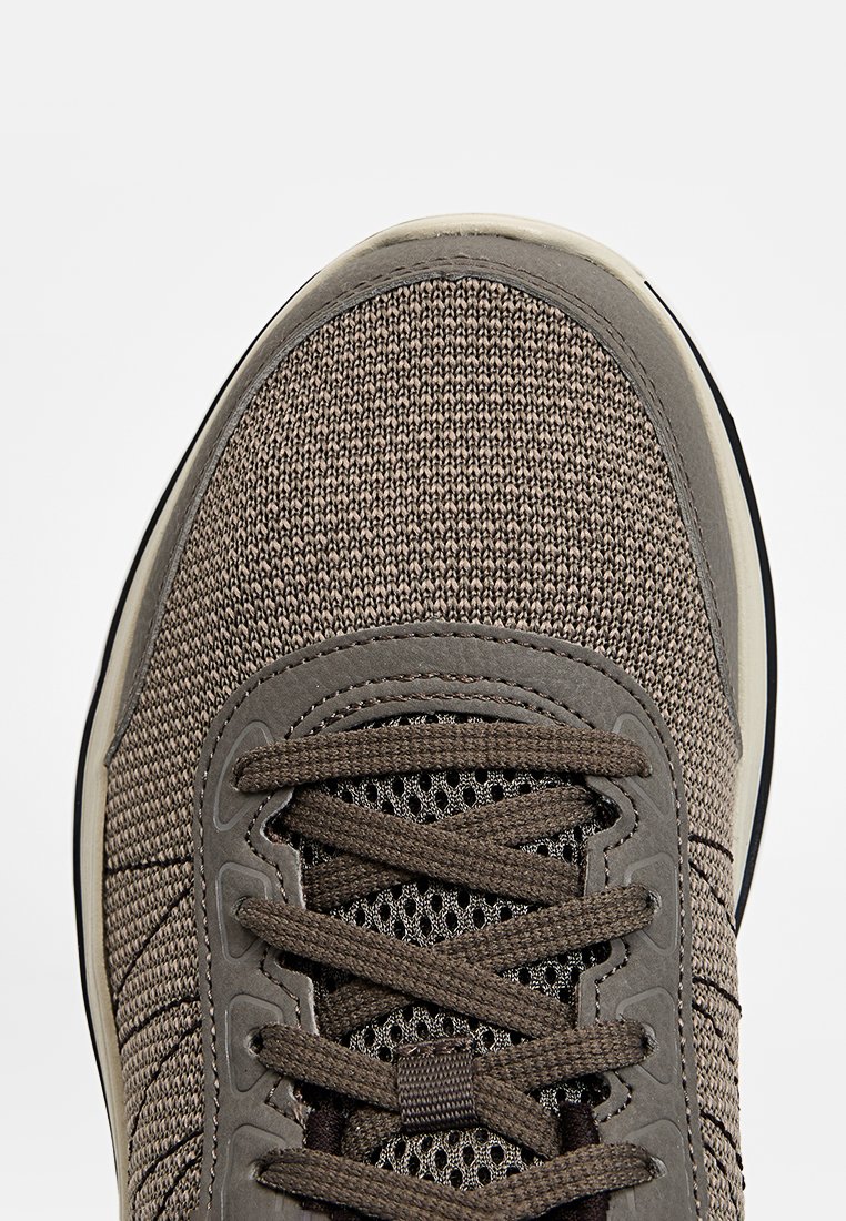 Brązowy, teksturowany sneaker z plecioną cholewką, zamszowymi akcentami i płaskimi sznurowadłami. Posiada amortyzowaną podeszwę i siateczkowe panele dla wentylacji.