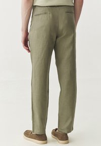Licht olijfgroene linnen broek met een relaxed fit, rechte pijpen en twee achterzakken. Gedragen met beige instapschoenen.