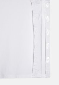 T-shirt blanc avec une texture lisse et un bord décoratif en dentelle le long des deux côtés, accentué de découpes en motif diamant.