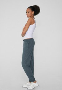 Dunkelblaue Jogginghosen mit elastischem Bund und Kordelzug, kombiniert mit einem figurbetonten weißen Tanktop und weißen Turnschuhen.