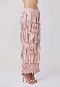 Jupe à franges rose en tissu texturé. Chaque couche est ornée de franges étroites, dotée d'une taille élastique et d'une longueur maxi. Associée à des talons blancs.