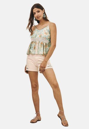 Top peplum floral en azul claro y naranja, con borde de encaje; combinado con pantalones cortos rosas con recortes florales y sandalias planas con tiras.