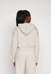 Light beige cropped hoodie with a hood and long sleeves, featuring a ribbed hem and white side stripes, made from soft cotton material.