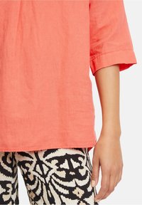 Top in lino corallo con maniche piegate abbinato a pantaloni a patterned bianco e nero con design floreale.
