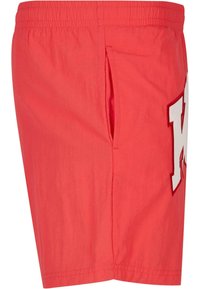 Red shorts made of lightweight fabric, featuring a side pocket and a white letter "K" appliqué on the leg. Smooth texture and elastic waistband.