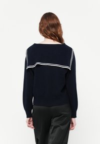 Pull bleu marine avec un large col replié comportant des rayures blanches. Le design présente des manches longues et un ourlet ajusté, fabriqué à partir d'un matériau tricot doux.