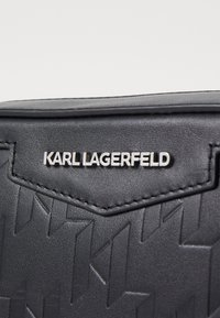 Schwarze strukturierte Lederhandtasche mit geprägtem geometrischem Muster. Silbernes "KARL LAGERFELD"-Logo, das auf der Vorderseite prominent platziert ist.