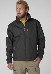 Chaqueta negra impermeable con cremalleras rojas, diseño de cuello alto y textura ligera. Incluye bolsillos laterales y una marca en la manga.