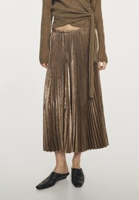 Gonna midi plissettata in velluto marrone indossata con un maglione corto marrone e scarpe slip-on nere con punta quadrata.