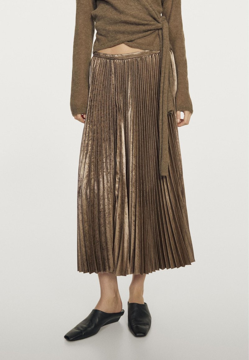 Gonna midi plissettata in velluto marrone indossata con un maglione corto marrone e scarpe slip-on nere con punta quadrata.