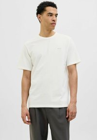 Tricou alb cu mânecă scurtă, fabricat dintr-un material moale, având un guler rotund și un logo mic, discret pe piept. Croiala este lejeră.
