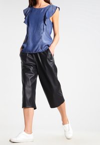 Denim top with ruffled sleeves, paired with black leather culottes and white slip-on shoes. Features a relaxed fit and simple design.
