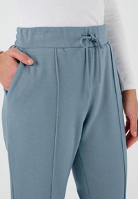 Joggers suaves en azul con cintura elástica y cordón, que cuentan con bolsillos laterales y un diseño ajustado. Textura lisa con detalles de costura.