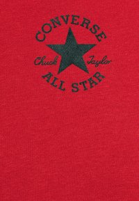 Camiseta roja hecha de tejido texturizado con un logo de estrella negra que incluye el texto "CONVERSE" y "ALL STAR" en impresión negrita.