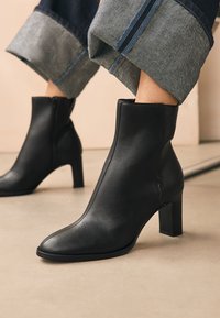 Schwarze knöchelhohe Lederstiefel mit spitzer Zehenpartie und Blockabsatz. Das Design zeichnet sich durch eine glatte Oberfläche und einen seitlichen Reißverschluss für einfaches An- und Ausziehen aus.