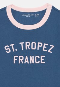 Hellblaues Baumwoll-Baby-T-Shirt mit einem rosa gerippten Kragen. Auf der Vorderseite prangt "ST. TROPEZ FRANCE" in weißen, gestickten Buchstaben. Größe 13/14.