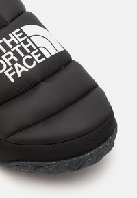 Scarpa nera e gonfia con superficie testurizzata, caratterizzata da un logo bianco. La suola è robusta con un motivo maculato, progettata per garantire aderenza.