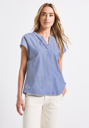Chemise à rayures bleu clair à manches courtes avec un col et une patte de boutonnage demi-longueur, fabriquée en tissu respirant. Portée avec un pantalon couleur crème.