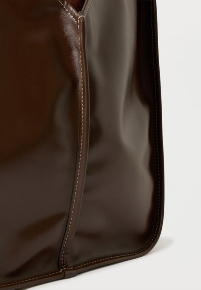Barna bőrtáska sima felülettel, kontrasztos varrással az élein és struktúrált formával. Minimalista dizájn.