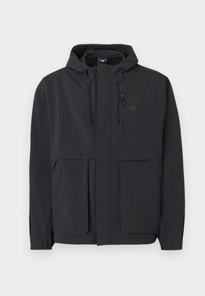 Veste légère noire avec capuche, fermeture éclair frontale, poche zippée sur la poitrine, deux grandes poches frontales à rabat et réglage de la capuche par cordon.