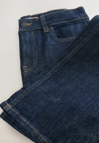 Dunkelblå denim jeans, der er foldet pænt, med en knaplukning, kontrasterende gul syning og et klassisk femlomme-design.