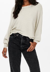 Pull crème clair côtelé avec une coupe ample et des manches larges, associé à un jean noir taille haute avec un léger délavage et un design classique.