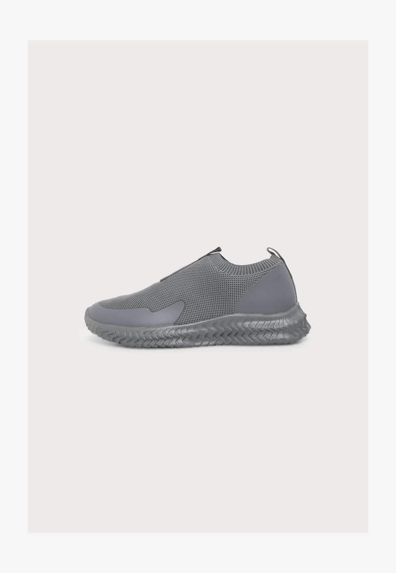 Γκρι sneaker χωρίς δεσίματα με υφή πλεκτού επάνω μέρους, ριμπ γιακά, ταινία έλξης στη φτέρνα και μοτίβο ευέλικτης σόλας σε λευκό φόντο.
