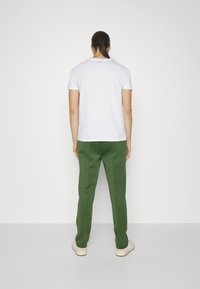 Witte korte mouwen t-shirt en groene broek; gestructureerde stof; losse pasvorm; gecombineerd met lichte schoenen. Achteraanzicht zonder extra details.