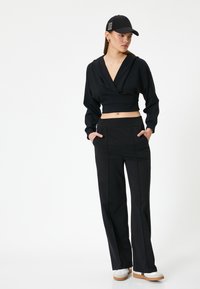 Schwarzer, verkürzter Hoodie mit tiefem V-Ausschnitt und weiten Ärmeln, kombiniert mit schwarzen, weiten Hosen mit elastischem Bund und Taschen.