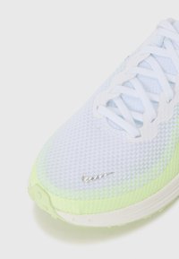 Leichte Sportschuhe mit einem weißen Mesh-Obermaterial, limonengrünen Akzenten, strukturiertem Design und silbernem Logo an der Seite.