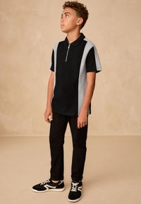 Černé a světle šedé polo tričko s krátkým rukávem a límcem na zip, doplněné černými kalhotami a černými teniskami s bílými detaily.