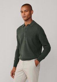 Tamnozeleni pleteni polo majica s ovratnikom, pet dugmića i rebrastim manžetama. Nosila se s svijetlosmešnim hlačama. Glatka tekstura.