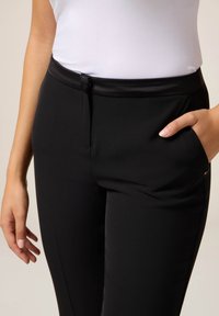 Pantaloni neri in tessuto morbido, con vita a gancio nascosto, tasche laterali e vestibilità sartoriale.