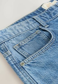 Jean en denim bleu avec une légère décoloration, dotée d'une poche avant, de coutures jaunes et d'un accent en bouton en métal. Design classique à cinq poches.