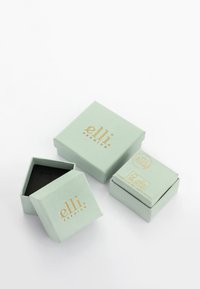 Cajas de joyería verdes y cuadradas con branding dorado, una abierta mostrando un interior negro. Papel texturizado y un diseño compacto.